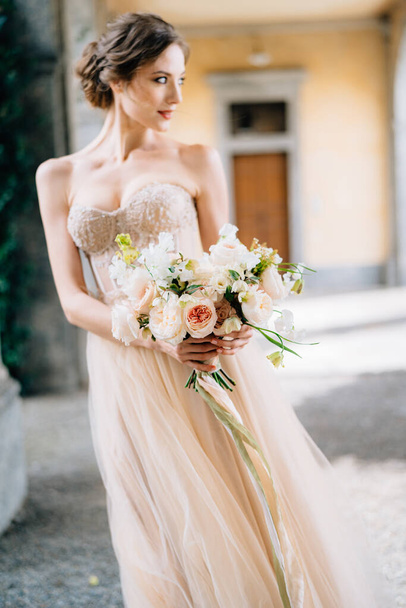 Νύφη σε ένα όμορφο φόρεμα με ένα μπουκέτο ροζ λουλούδια στέκεται στην θολωτή αίθουσα με το κεφάλι της γυρισμένο. Λίμνη Κόμο, Ιταλία. Κλείσε. - Φωτογραφία, εικόνα
