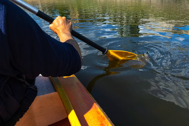 Gros plan d'une personne faisant du canot dans la rivière par une journée ensoleillée. Mains tenant une pagaie et ramant dans l'eau courante - Photo, image