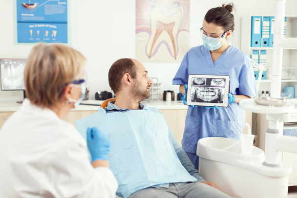 Хвора людина сидить на стоматологічному чаї, дивлячись на рентгенографію на цифровому планшеті
 - Фото, зображення