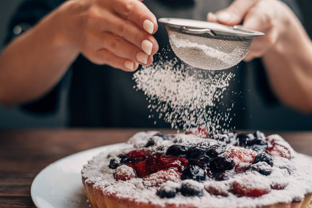 Unrecognizable woman sprinkles icing sugar on berry pie. - Photo, image