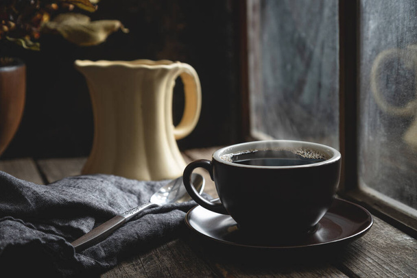 Cup of hot coffee on a rustic wooden table by a window - Фото, зображення