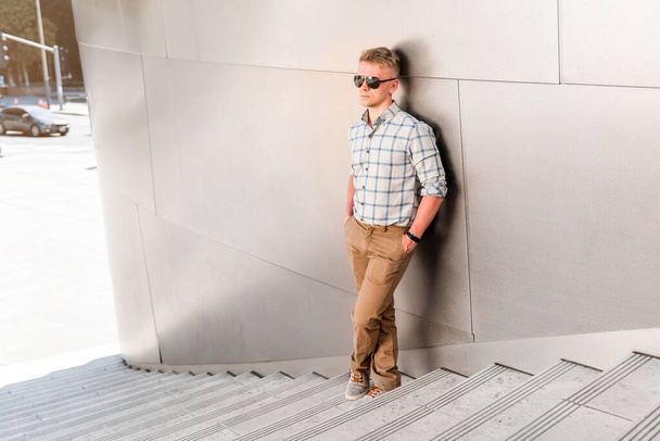 Młody blondyn w okularach przeciwsłonecznych stoi na schodach sali koncertowej Walta Disneya. Biznes styl w modnym budynku, Los Angeles - Zdjęcie, obraz