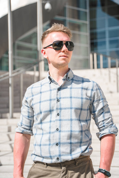 A young blond man in sunglasses stands on the steps of the Walt Disney Concert Hall. Business style in a trendy building, Los Angeles - Fotó, kép