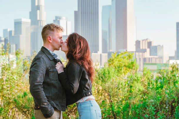 公園のベンチで早朝の若い男性と女性のロマンチックなデートロサンゼルスのダウンタウンの高層ビルを見下ろす - 写真・画像