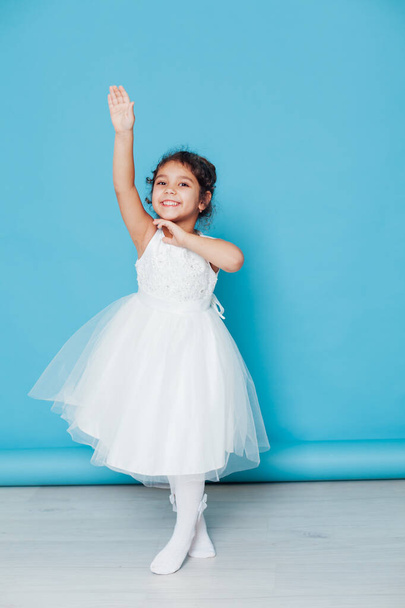Красивая маленькая девочка танцует под песню в белом платье на синем фоне - Фото, изображение