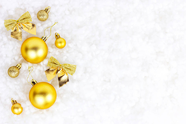 Bright golden and yellow Christmas decorations (ribbons, baubles, ornament) flat lay on white artificial snow background with copy space. Christmas and New Year traditional holiday celebration concept. - Photo, Image