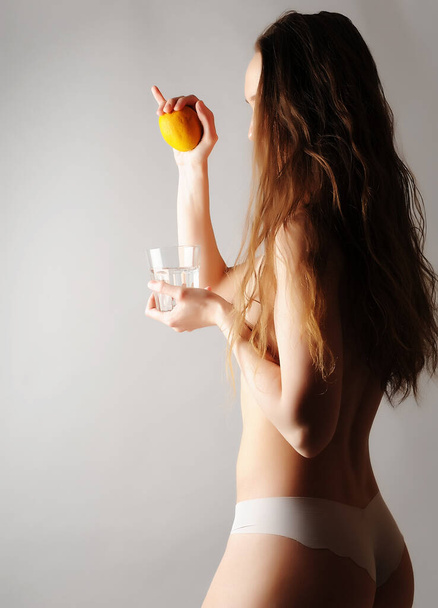 Boldog fiatal nő egy pohár vízzel és citrommal, világos szürke háttérrel. Egészséges életmód koncepció - Fotó, kép