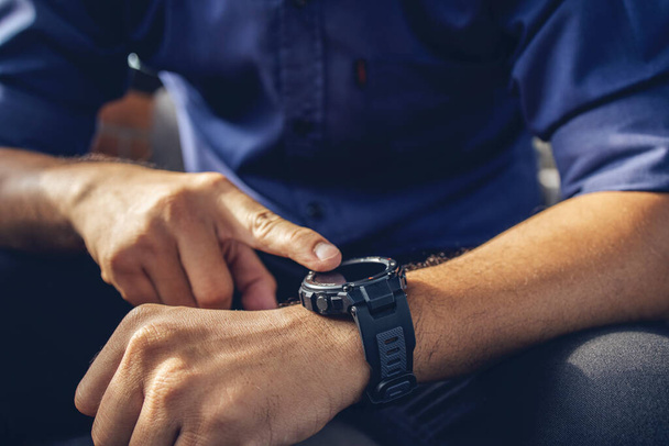 businessman wearing digital smart watch in hand  touching screen to open notification, read message and activity tracker in wrist with soft-focus and over light in the background. - Photo, Image