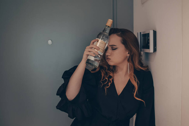 The drunk girl came home after the party. Beautiful woman on the doorstep tired with a bottle of alcohol. Alcoholism, drinking alone, alcohol headaches. - Photo, image
