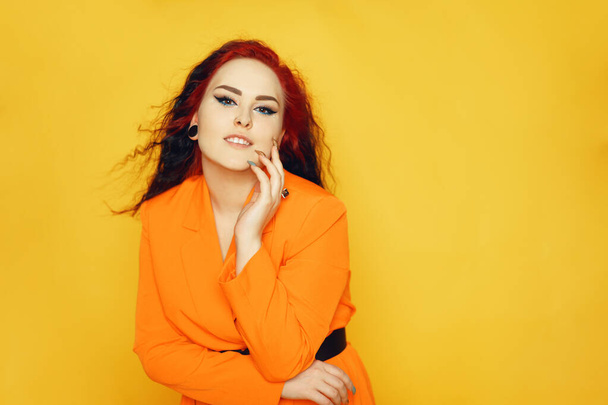 Beautiful girl on a yellow background. A brunette in an orange dress and long hair is posing, smiling, having fun. Summer photo woman in studio. Joy and emotion. Red hair roots place for text. - Foto, imagen