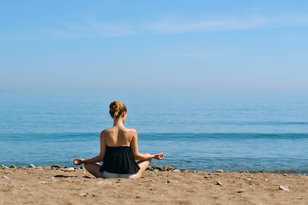 Uma menina bonita está envolvida em ioga na praia contra o fundo do mar. Saúde e desporto. Uma mulher na costa do oceano medita e relaxa. Verão e viagens. - Foto, Imagem