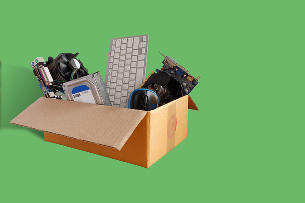 Discos rígidos e placas-mãe e acessórios de hardware de computador antigos, resíduos eletrônicos em caixas de papel isoladas em fundo verde, conceito de reutilização e reciclagem. - Foto, Imagem