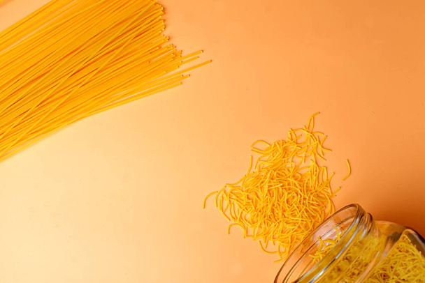 Scattered vermicelli on a peach background and spaghetti. - Foto, afbeelding