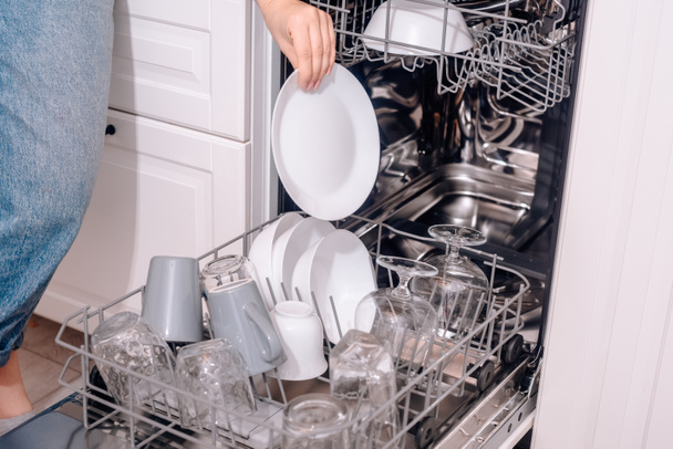 Sisäänrakennettu astianpesukone, tiskikone. Nainen lataa pestyjä astioita, kuppeja, laseja. Naisen lempeä käsi laittaa jotain astianpesukoneeseen tai vetää ulos, purkaa. - Valokuva, kuva