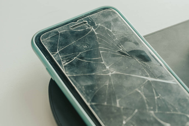 De mobiele telefoon ligt op tafel. Smartphone met gebroken scherm, glas. Schermreparatie, glasvervanging, reparatie. - Foto, afbeelding