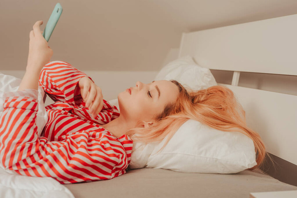 Egy lány reggel ránéz a telefonra, egy nő az ágyban videót néz, vagy híreket olvas. Internetfüggőség. - Fotó, kép