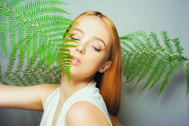 Beautiful young blond woman with perfect skin and natural make up posing front of plant tropical green leaves background. Teen model hair care of her face Fashion. - Zdjęcie, obraz