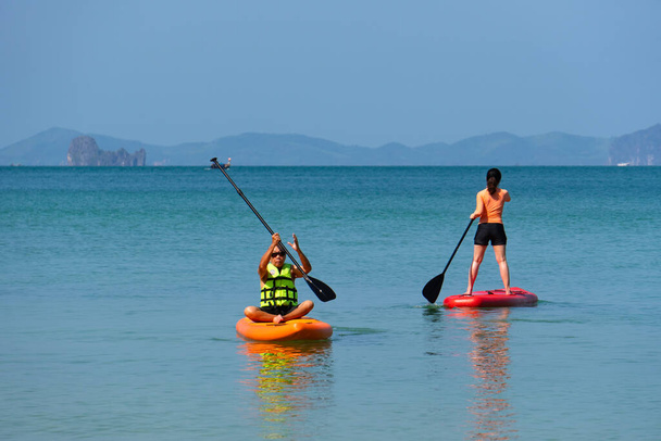 asiático padre mayor jugando de pie paddleboard o SUP con joven hija en azul mar en vacaciones de verano. familia juntos concepto - Foto, imagen