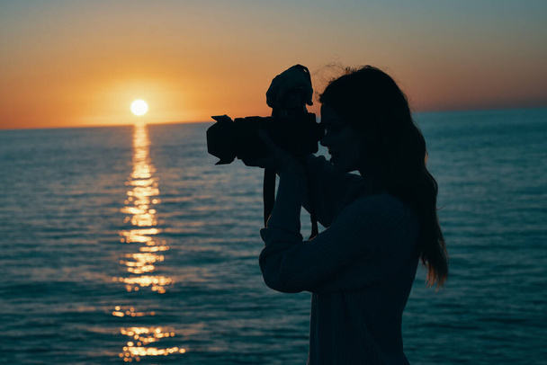 Fotografin mit Kamera bei Sonnenuntergang in der Nähe der Meereslandschaft - Foto, Bild