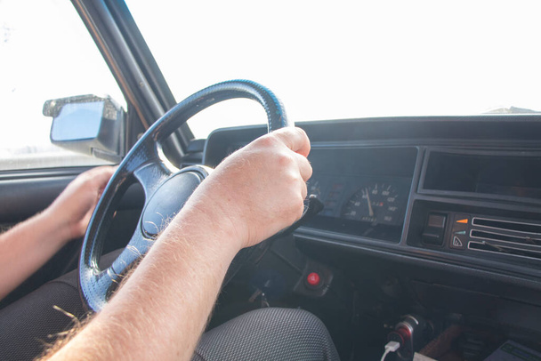 αρσενικά χέρια στο τιμόνι ενός παλιού σοβιετικού αυτοκινήτου στο δρόμο προς τον ήλιο κοντά - Φωτογραφία, εικόνα