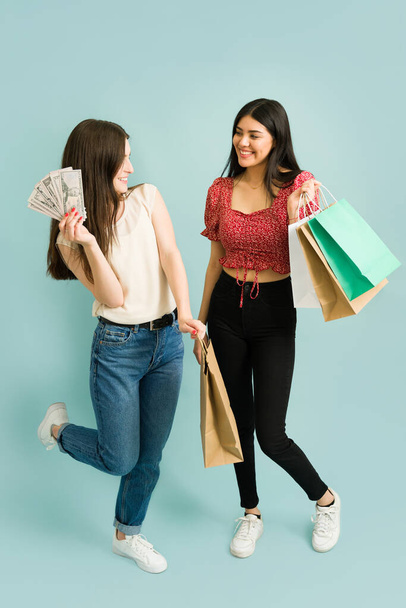 Longitud completa de dos mujeres jóvenes atractivas con bolsas de compras que llevan un montón de dinero en efectivo y el gasto en ropa en el centro comercial - Foto, imagen