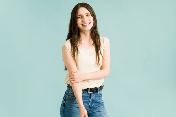 Portrait of a tender young woman looking shy while smiling. Woman in her 20s in casual clothes looking happy against a colorful background - Foto, afbeelding