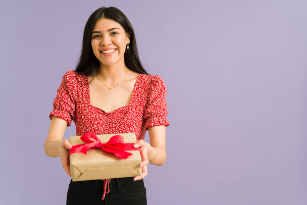 Liebevolle junge Frau aus Lateinamerika macht ein schönes Geburtstagsgeschenk und lächelt dabei vor violettem Hintergrund - Foto, Bild