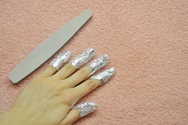 Quitar la goma laca de las uñas. dedos con papel de aluminio y lima de uñas sobre un fondo rosa. De cerca la mano. Vista frontal. - Foto, Imagen