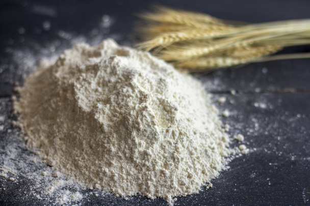 Una pila de harina en una mesa oscura y espigas de trigo en el fondo - Foto, imagen