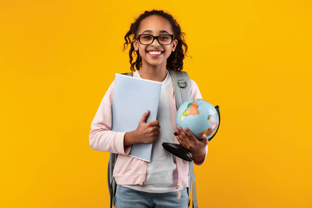 Vrolijk jong zwart meisje houden aarde wereld bol en notebook - Foto, afbeelding