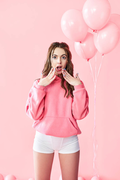Young trendy surprised woman with pink balloons on pink pastel background - Photo, Image