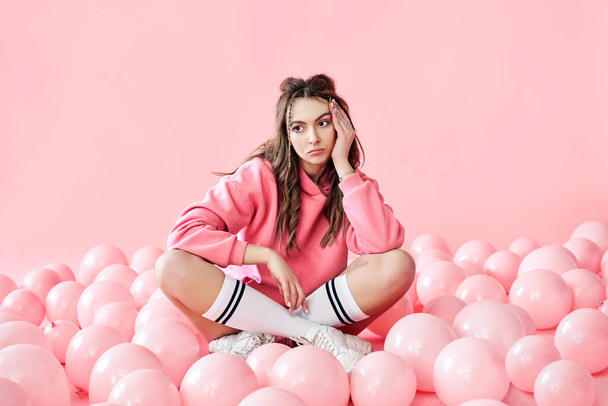 Bored fashionable woman sitting on floor with pink air balloons on pink pastel background - Fotografie, Obrázek