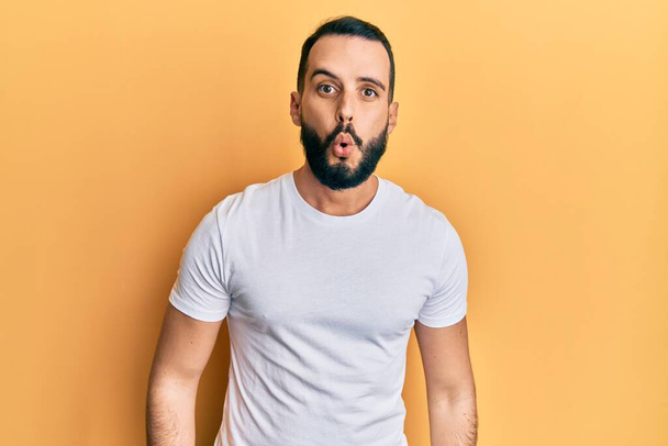 Young man with beard wearing casual white t shirt scared and amazed with open mouth for surprise, disbelief face  - Photo, Image