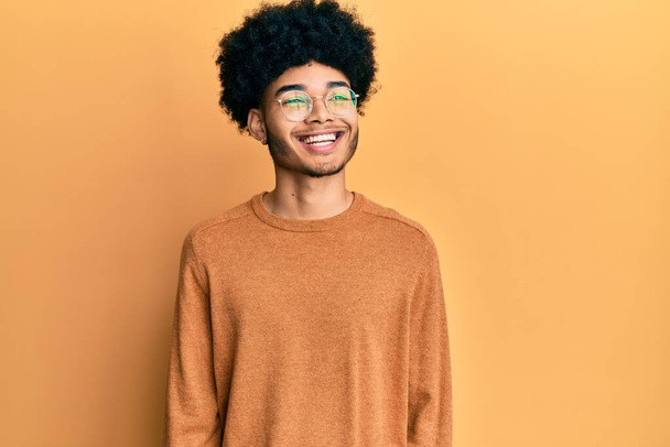 Νεαρός Αφροαμερικάνος με αφρο μαλλιά που φοράει casual χειμωνιάτικο πουλόβερ που κοιτάζει αλλού με χαμόγελο στο πρόσωπο, φυσική έκφραση. γελώντας σίγουρος.  - Φωτογραφία, εικόνα