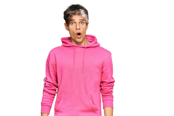 Fiatal spanyol férfi visel alkalmi rózsaszín pulóver fél és megdöbbent meglepetés kifejezés, félelem és izgatott arc.  - Fotó, kép