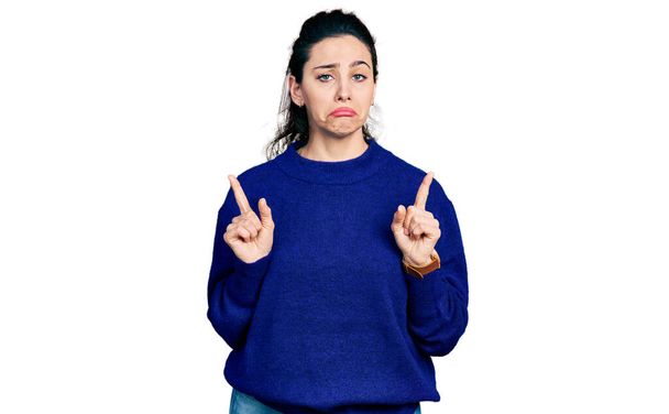 Mujer hispana joven con ropa casual señalando hacia arriba mirando triste y molesto, indicando la dirección con los dedos, infeliz y deprimido.  - Foto, Imagen