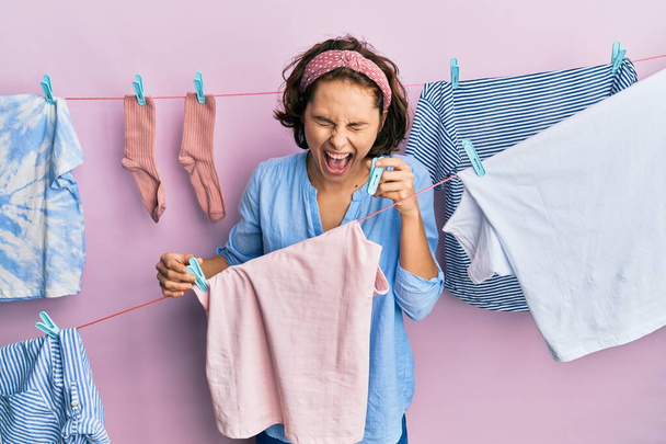 若いですブルネット女性行う洗濯保持ピンセット笑顔と笑いハードアウト大声でなぜなら面白いクレイジー冗談.  - 写真・画像