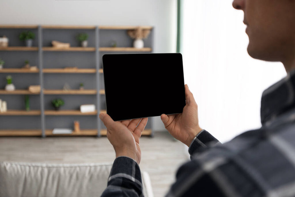 Guy Holding Tablet con schermo vuoto su sfondo soggiorno - Foto, immagini
