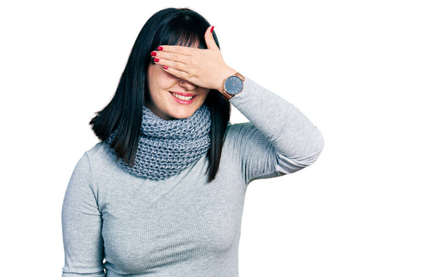 Mladá hispánka plus velká žena v zimní šále se usmívá a směje se s rukou na tváři, aby zakryla oči překvapením. slepý koncept.  - Fotografie, Obrázek
