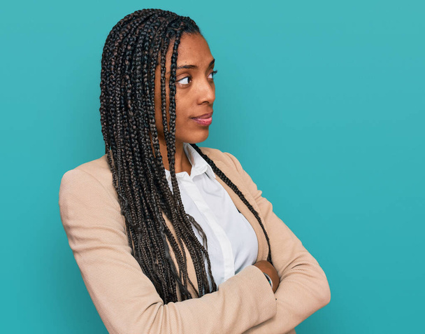 Mujer afroamericana vistiendo chaqueta de negocios mirando a un lado con los brazos cruzados convencida y confiada  - Foto, imagen