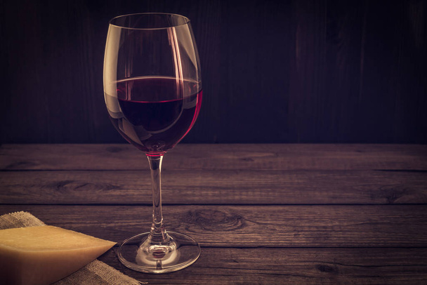 Glass of red wine with a piece of parmesan on an old wooden table - Foto, immagini