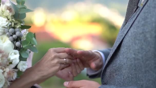 Bride holds bouquet and puts ring on grooms finger during wedding ceremony - Footage, Video