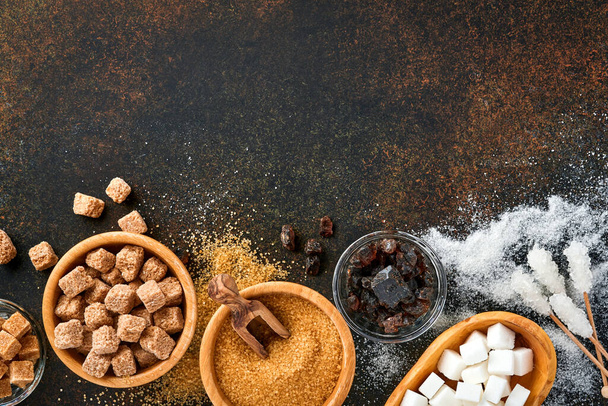 White sugar, cane sugar cubes, caramel in bamboo bowl on dark brown table concrete background. Assorted different types of sugar. Top view or flat lay. - Zdjęcie, obraz