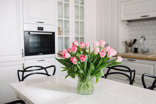 Boeket roze tulpen in een transparante vaas, op keukentafel. Bloemen in het interieur. - Foto, afbeelding