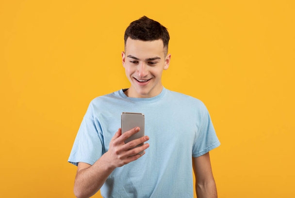 Cheerful young man using mobile phone, chatting online, having business meeting or webinar on orange background - Valokuva, kuva