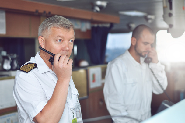 El capitán de un buque de carga con una camisa blanca y tirantes en el puente habla en un walkie-talkie. - Foto, imagen