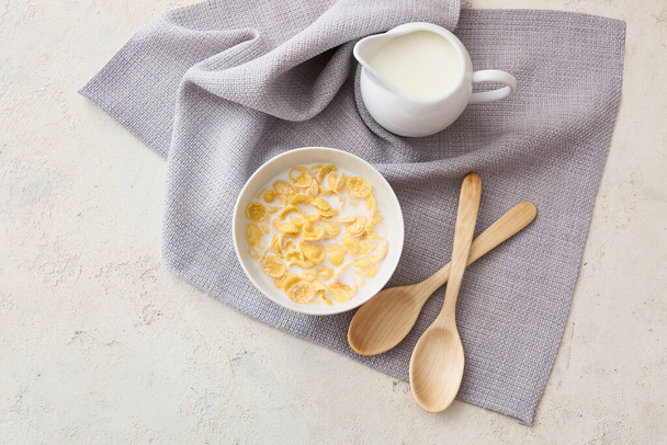 Bowl with tasty cornflakes and jug of milk on light background - Foto, Imagem