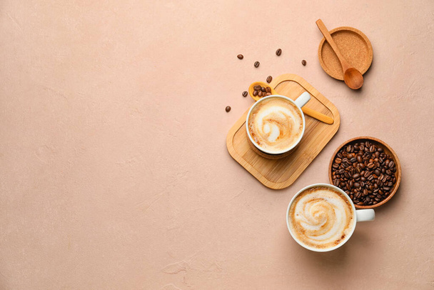 Чашки горячего капучино и тарелка с кофейными зернами на цветном фоне - Фото, изображение
