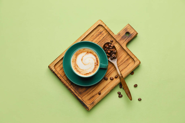 Coupe de cappuccino chaud et cuillère avec des grains de café sur fond de couleur - Photo, image