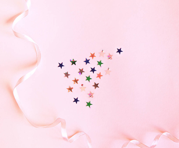 Shiny confetti of stars and round pieces on a pink background. Flat lay, top view. Decor with a thin pink ribbon. Festive background for your projects. - Foto, imagen